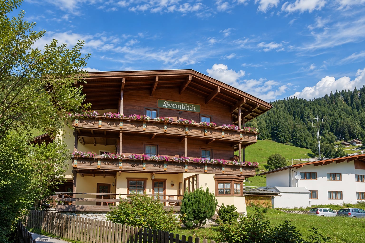 Haus Sonnblick in Lanersbach mit Schriftzug und Blumenbalkonen vor den grünen Hängen des Tuxertals