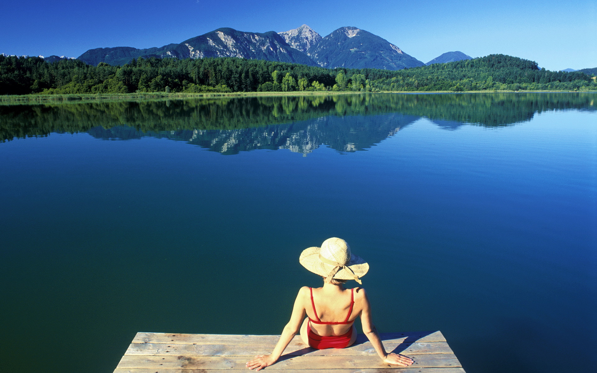 Frau mit Sonnenhut auf einem Steg am Turnersee mit Blick auf die Karawanken